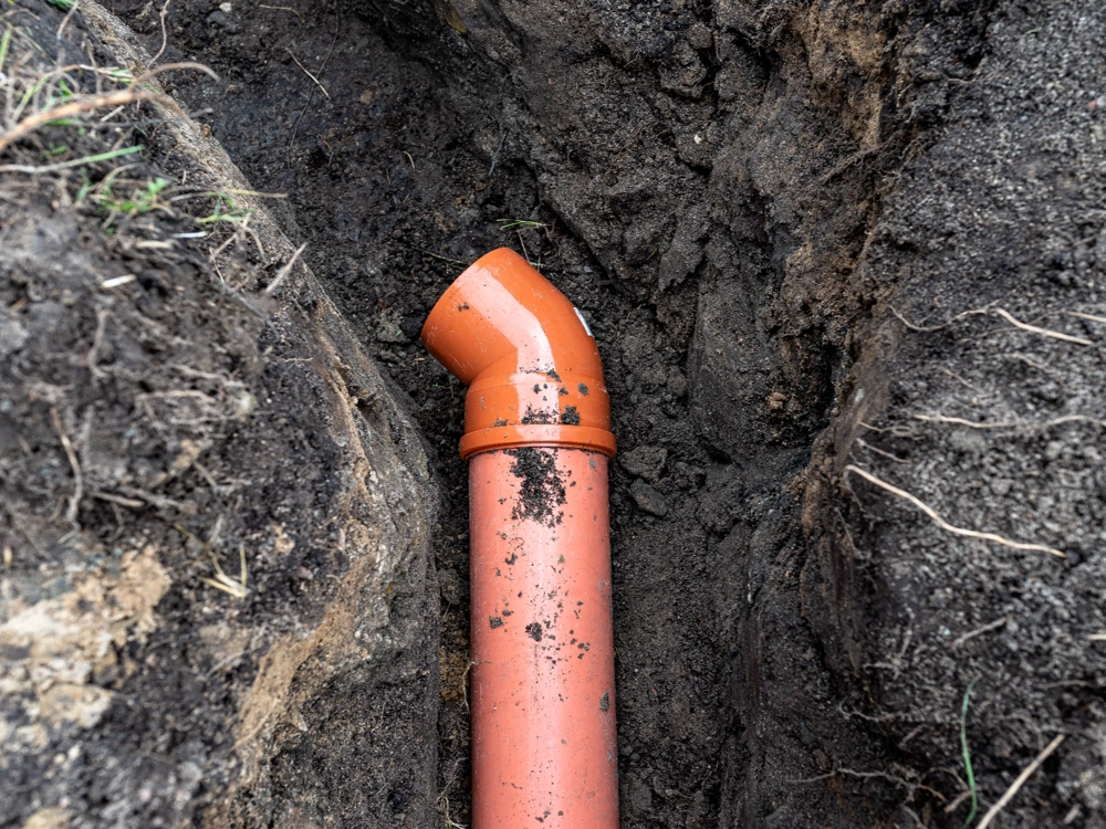 Pomarańczowa rura PCV z kolanem 45° osadzona w wykopie pod instalację WODKAN