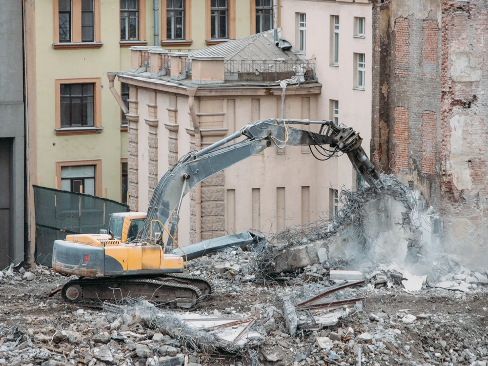 Koparka z młotem hydraulicznym rozbija ścianę budynku w trakcie wyburzeń