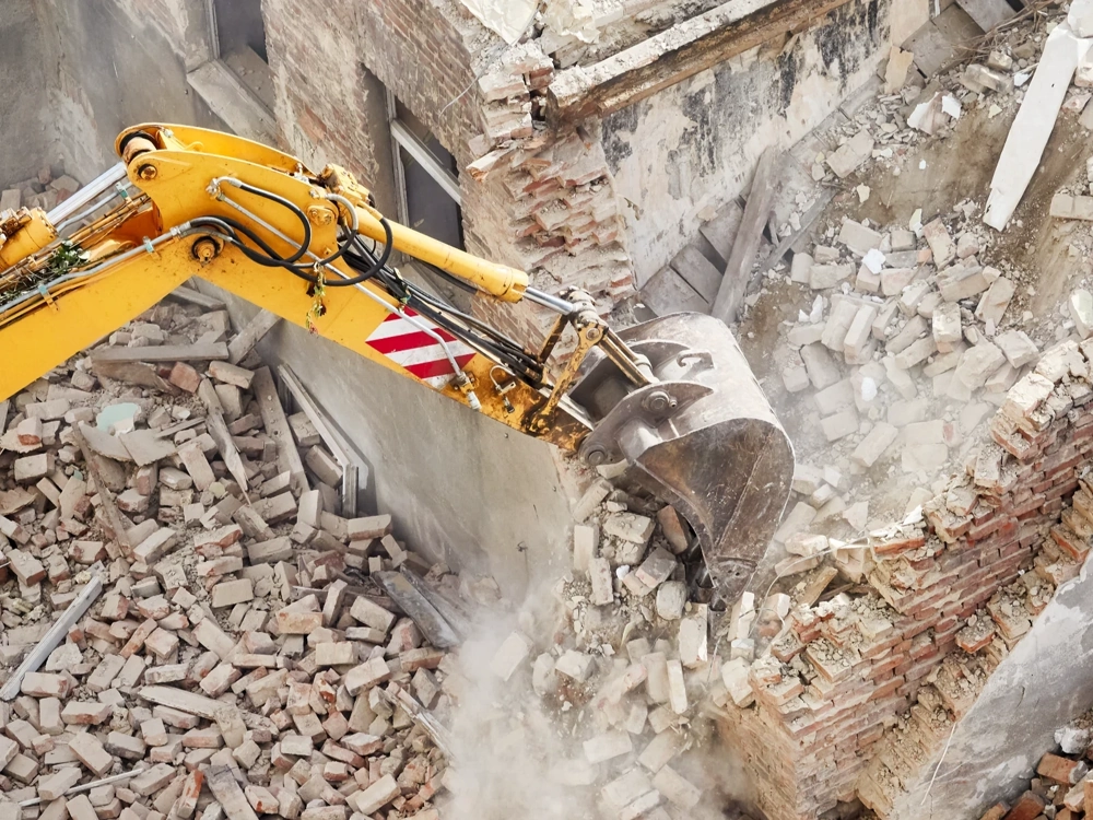 Żółty chwytak koparki wyburzający ceglany mur, gruz i odłamki na placu budowy - Wyburzenia