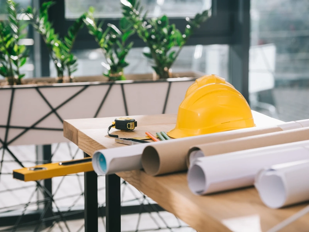 Stół z kaskiem ochronnym, taśmą mierniczą i zwiniętymi planami – wyposażenie pod Fit-out wnętrz