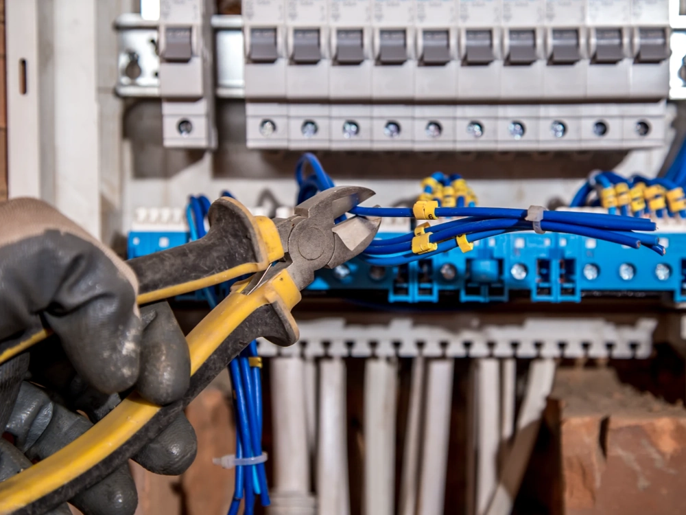 Elektryk przycinający niebieskie przewody w rozdzielnicy podczas instalacji elektrycznej